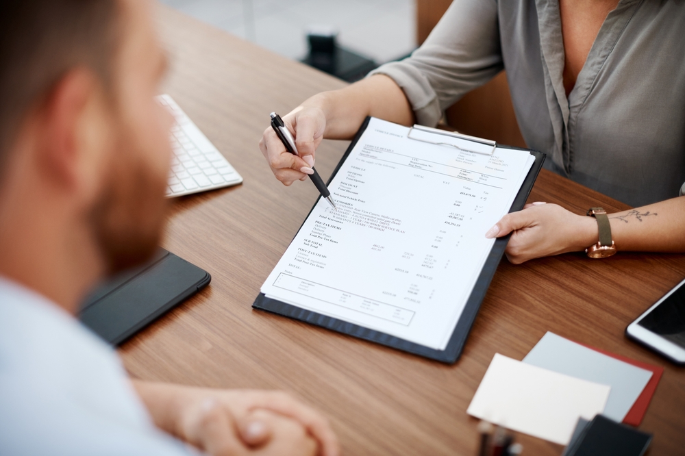 Man and client shaking hands over contract at desk, discussing insurance policy or sales agreement, with paperwork and application for signing