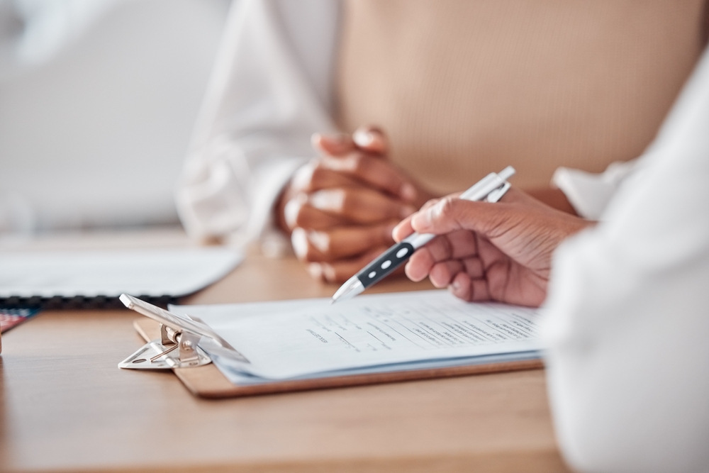 Hands holding a contract while doctor consults patient in hospital, writing medical history and discussing test results or healthcare advice.