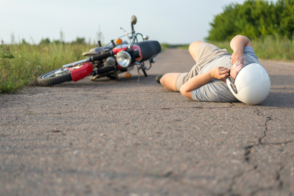 Injured man lying on asphalt beside fallen motorcycle, illustrating the aftermath of a road accident or motorcycle crash scene.