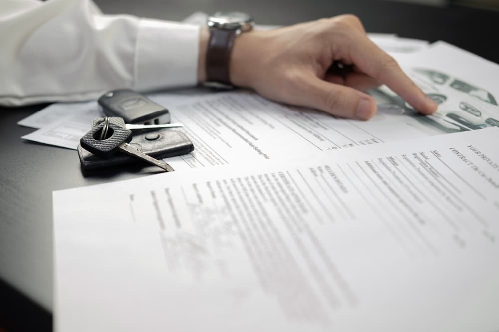 A person pointing at car insurance documents with car keys placed on the table.
