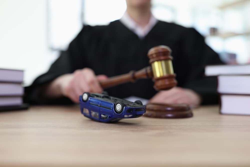 Judge holding a gavel with an overturned toy car on the desk, symbolizing a car accident case.