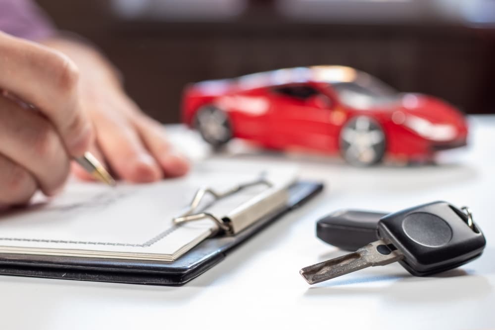 Person signing a document with car keys and a red toy car on the desk in focus.