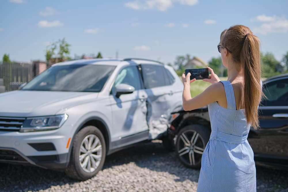 Woman taking photos of two cars involved in an accident on a sunny day.
