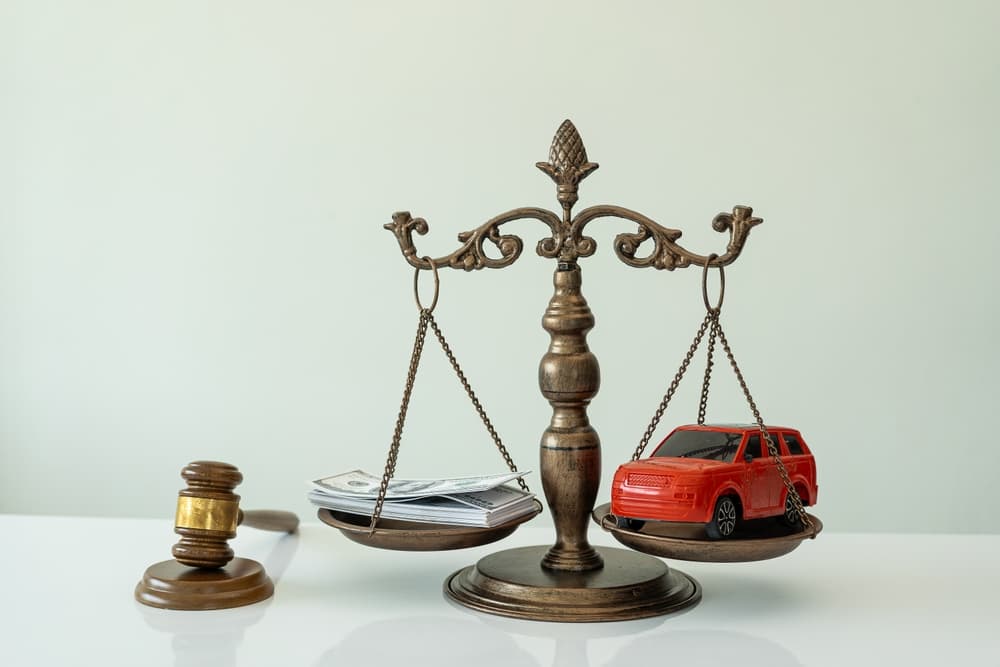 A scale balancing money and a toy car, with a gavel beside it.