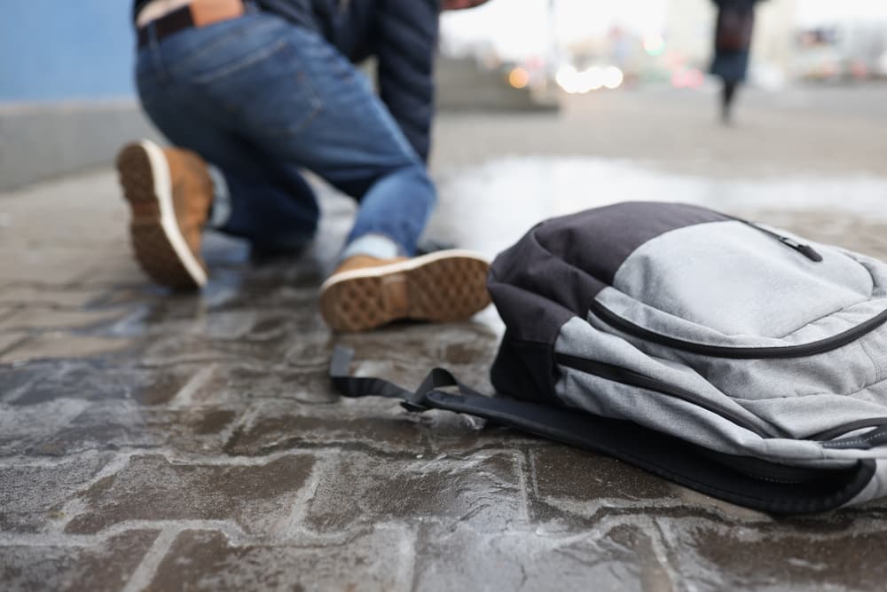 A person slipping on a wet sidewalk with a backpack lying nearby.