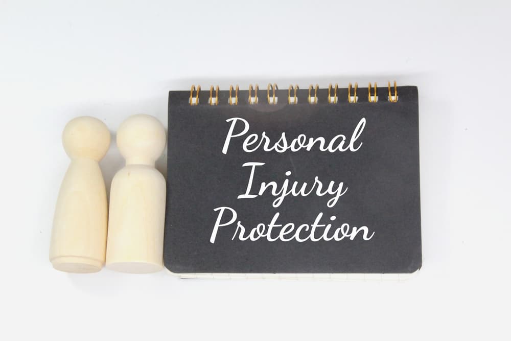 A notepad labeled "Personal Injury Protection" beside two wooden figures, symbolizing PIP insurance coverage.