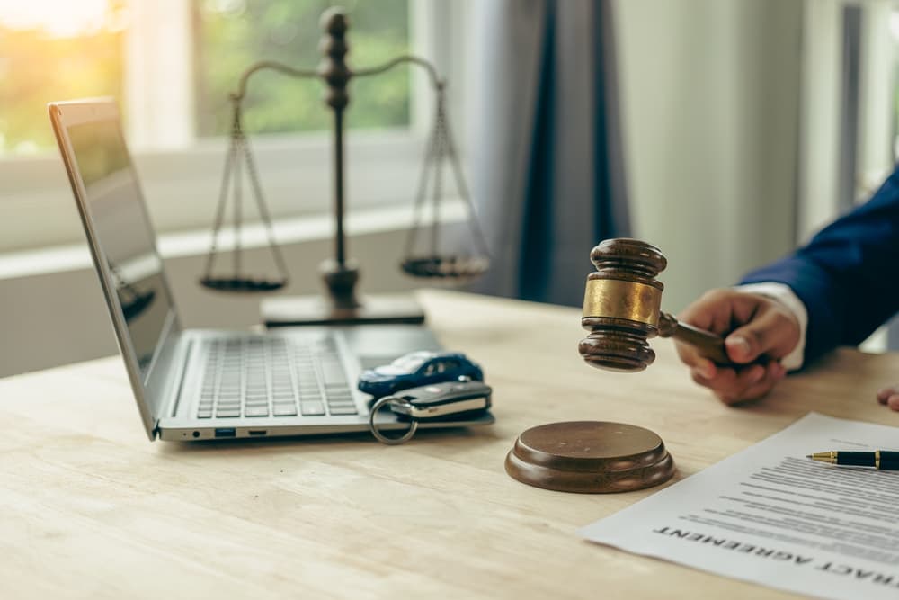 A lawyer holding a gavel near a laptop, scales of justice, and a legal document.