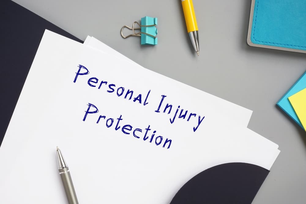 A document titled "Personal Injury Protection" on a desk with a pen, clip, and notebook.