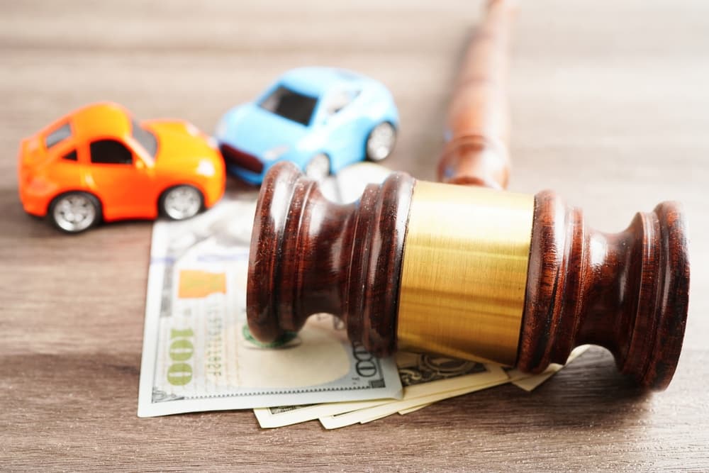 A gavel resting on dollar bills with two toy cars in the background, symbolizing legal and financial aspects of car accidents.