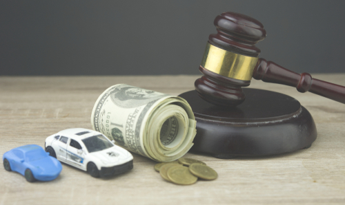 Two toy cars, a gavel, and rolled-up cash on a wooden surface, representing car accident legal fees.