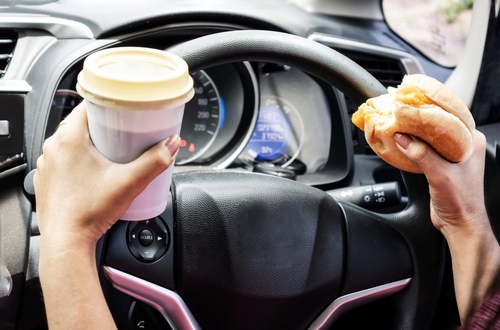 Driver holding a coffee cup in one hand and a sandwich in the other while driving