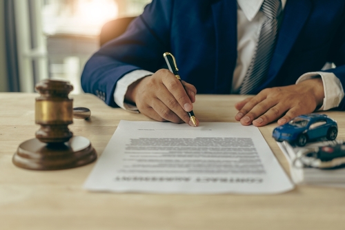 A lawyer signing a contract with a gavel and toy cars on the desk, illustrating legal representation for car accidents.