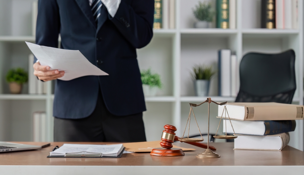Lawyer reviewing legal documents beside scales of justice in a modern office, reflecting case analysis, legal strategy, and professional consultation.