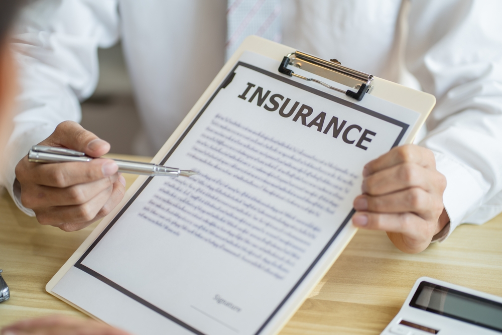 Insurance adjuster inspecting damaged car while agent reviews application form; toy cars simulate accident to assess insurance loss and claim process.