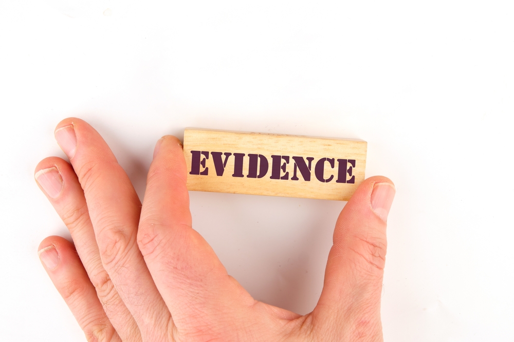Top view of hand assembling wooden blocks spelling EVIDENCE, symbolizing criminal investigation, fingerprint analysis, and forensic procedures.