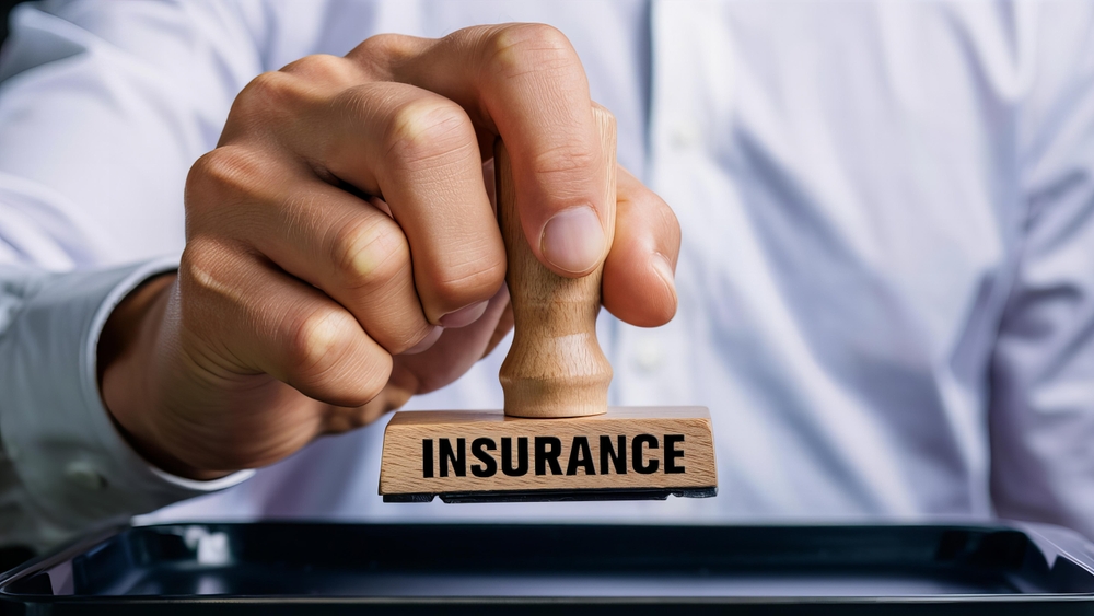 Close-up of hand holding rubber stamp with the word 'Insurance', symbolizing policy approval, coverage verification, or claim authorization.