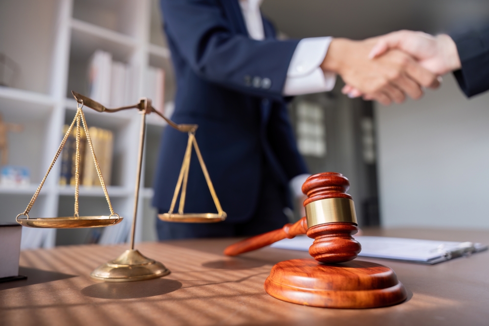 Professional lawyer handshake in modern office with justice scales and gavel on desk, symbolizing legal agreement, partnership, and trust