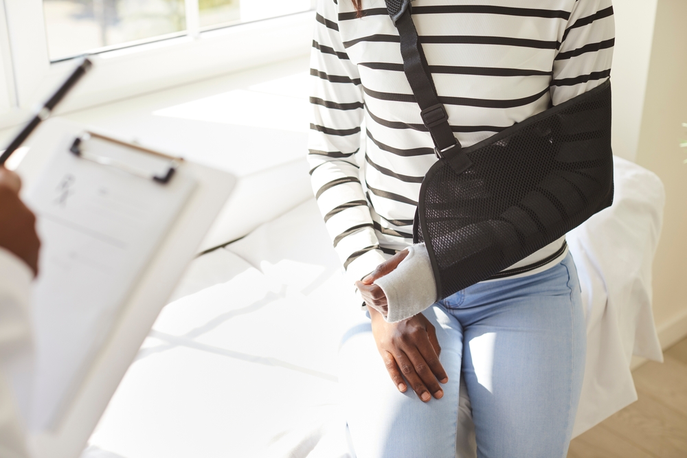 African American woman with arm in black sling discussing injury with doctor during medical consultation, injury recovery concept.