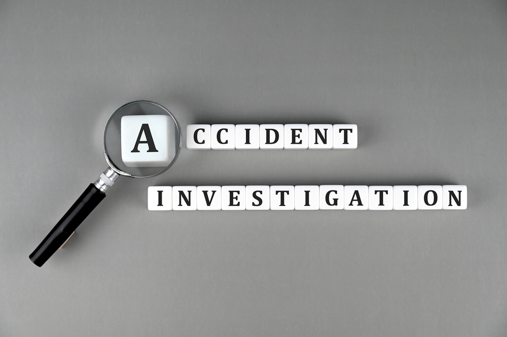 White lettered cubes spelling 'Accident Investigation' under a magnifying glass, symbolizing close examination of accident evidence.