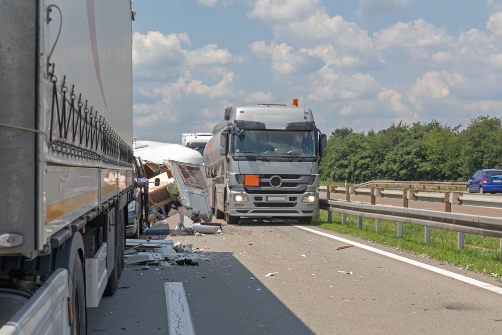 Semi trucks and camper trailer involved in traffic accident on highway with visible damage and emergency response activity.